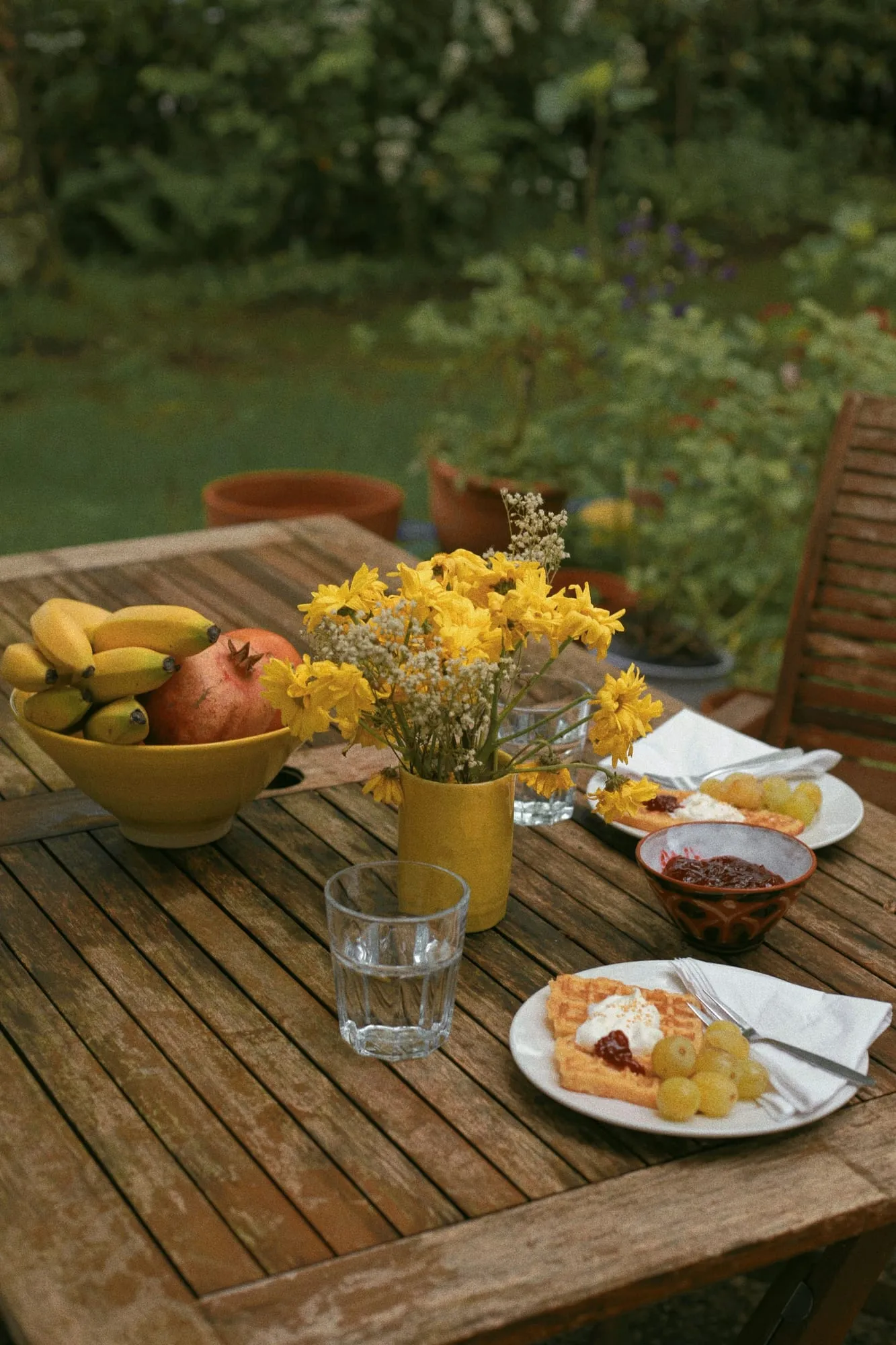 Frühstückstisch mit Obst und gelben Blumen im grünen Garten