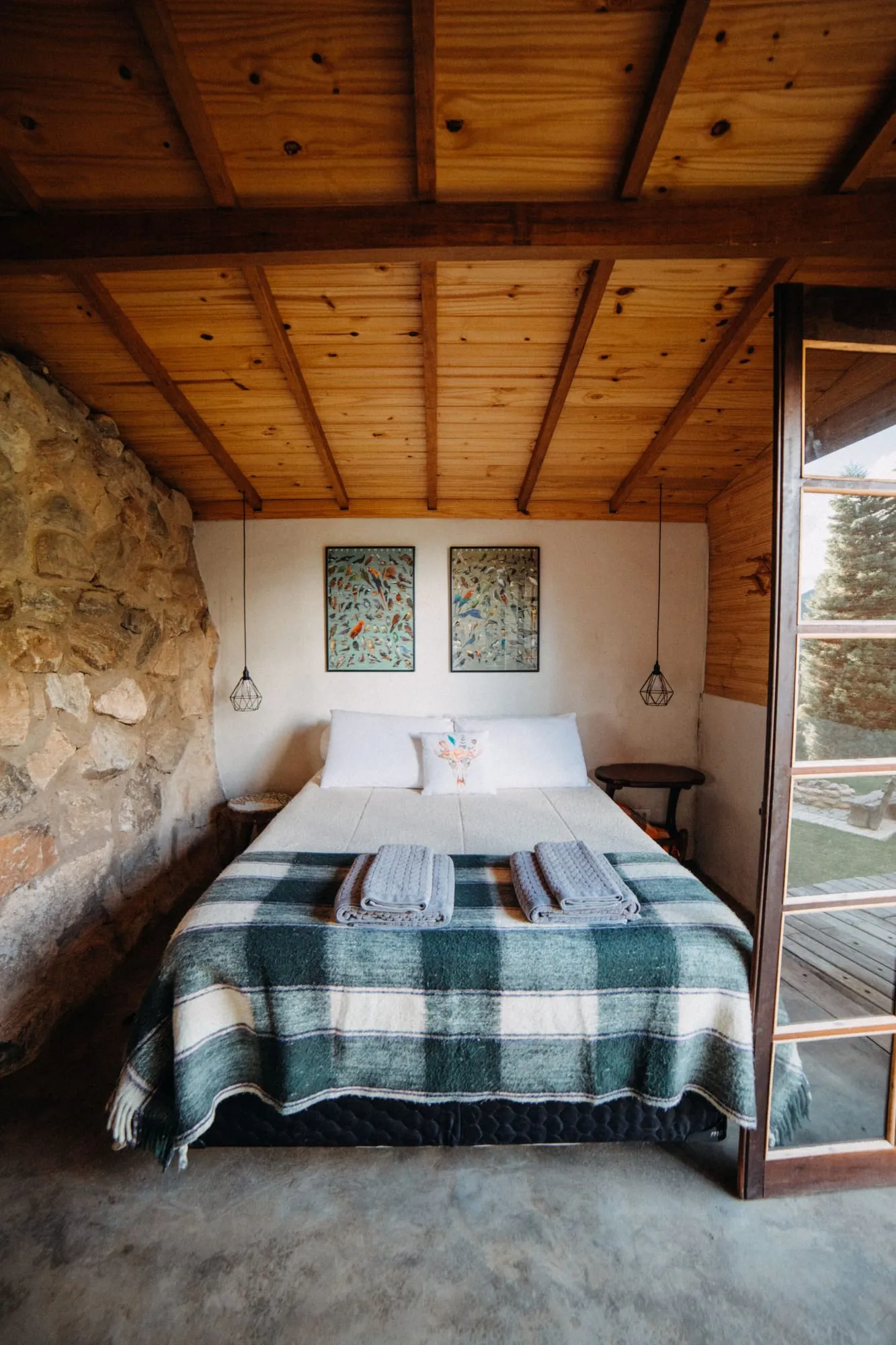 Bett mit karierter Decke unter einer Holzdecke neben einer Steinwand